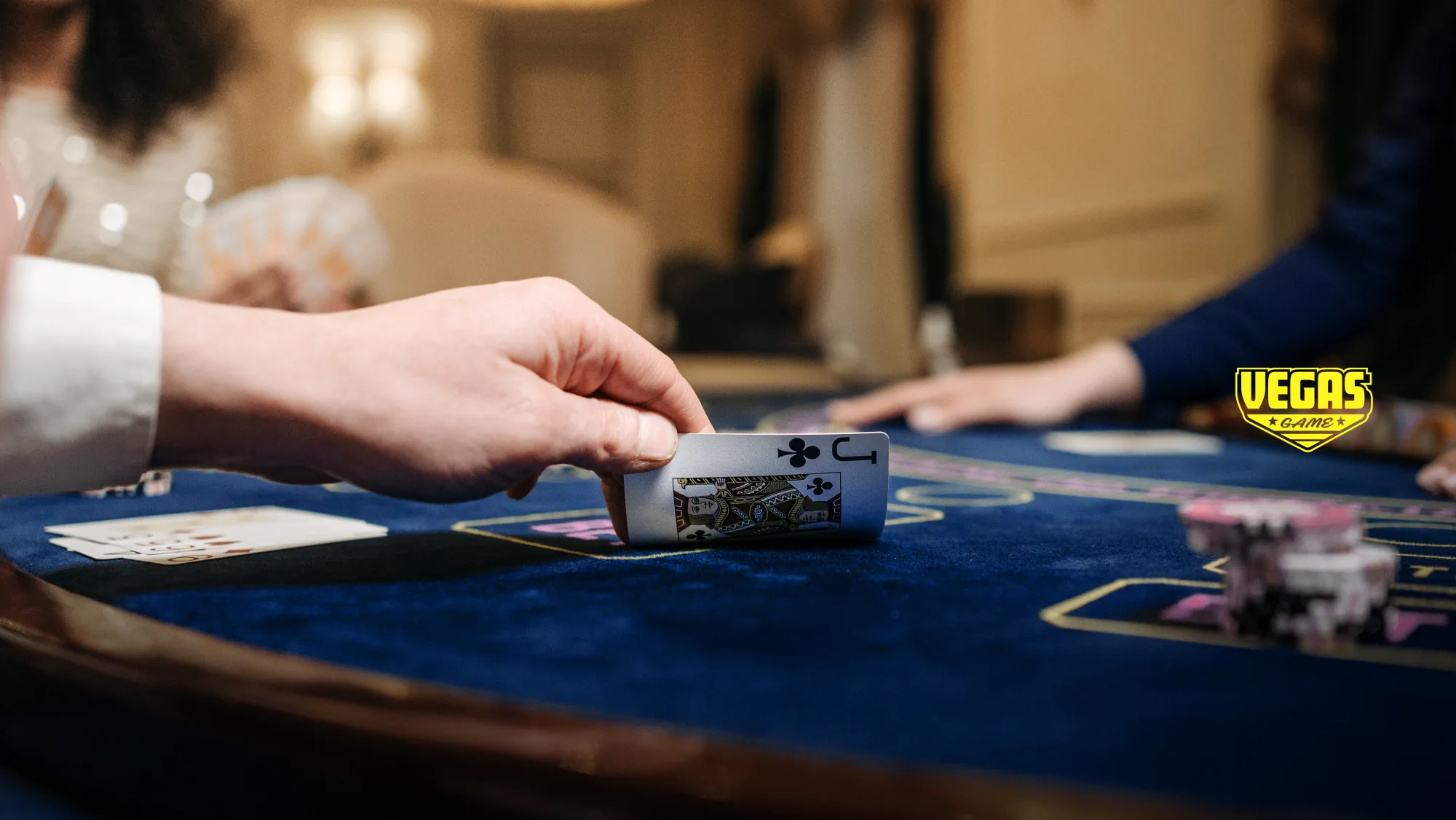 Vegas Game — main posant un valet de trefle sur une table de blackjack, logo jaune